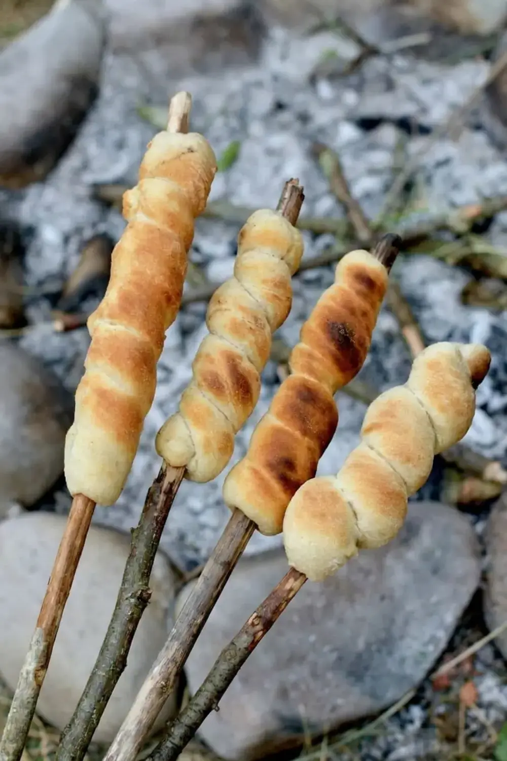 Stickbread positioned over hot campfire embers