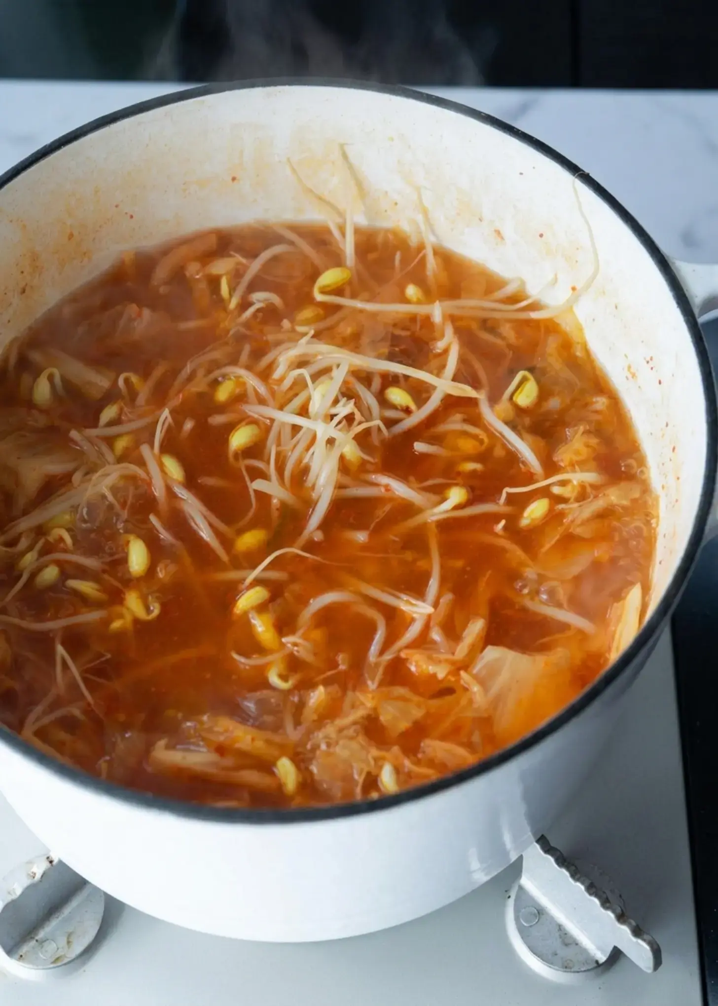 Soft tofu cubes being added to kimchi bean sprout soup